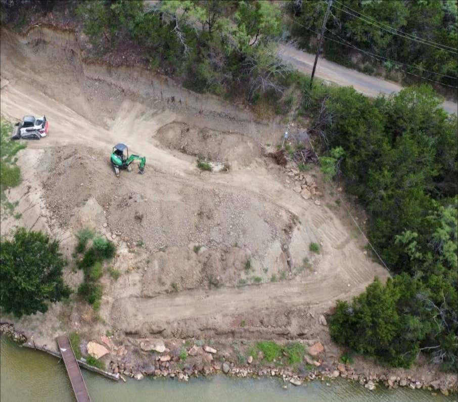 Aerial of the raw hillside cut, with an excavator and skid steer